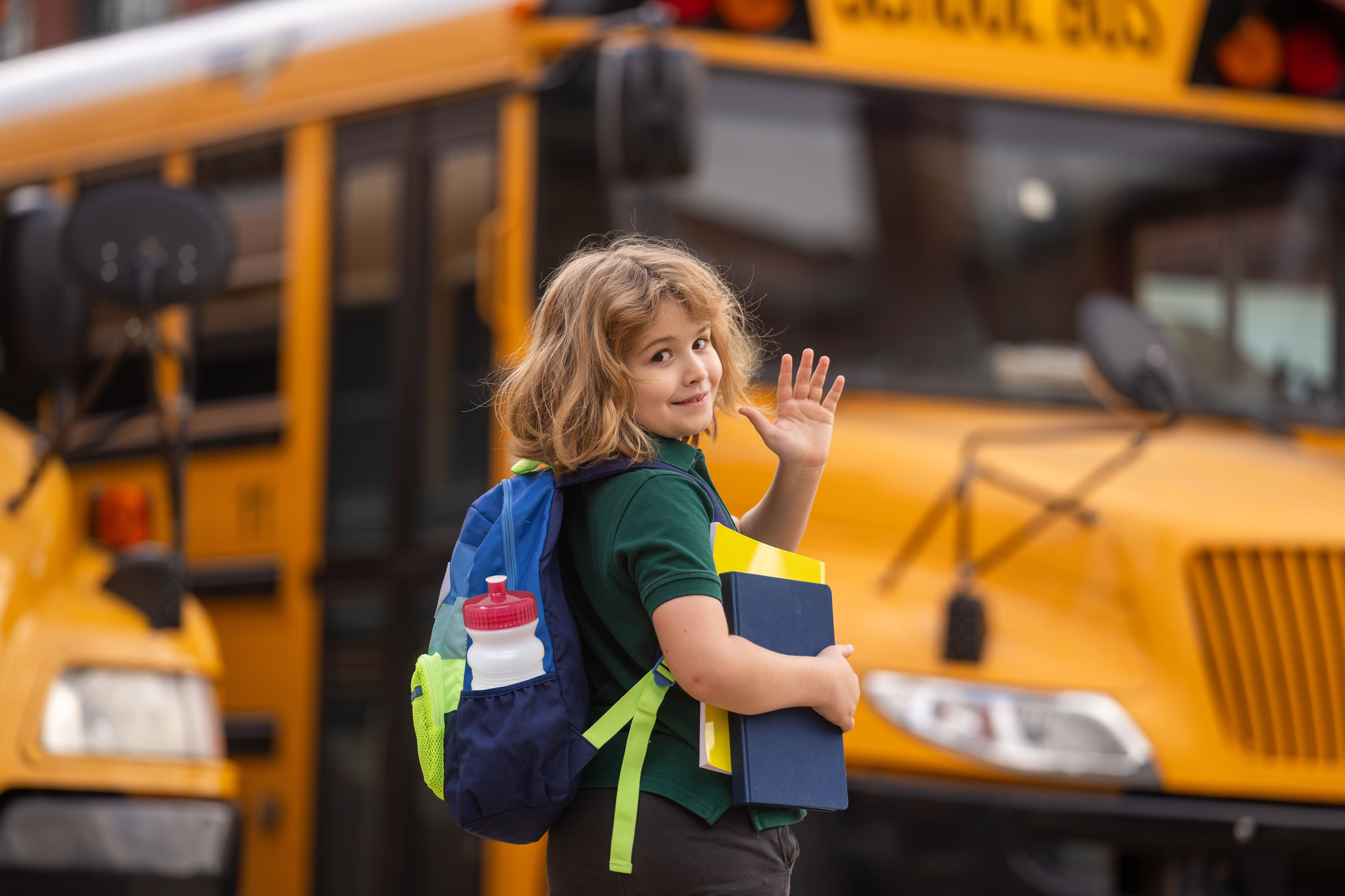 Young boy getting on school bus with water bottle in backpack.