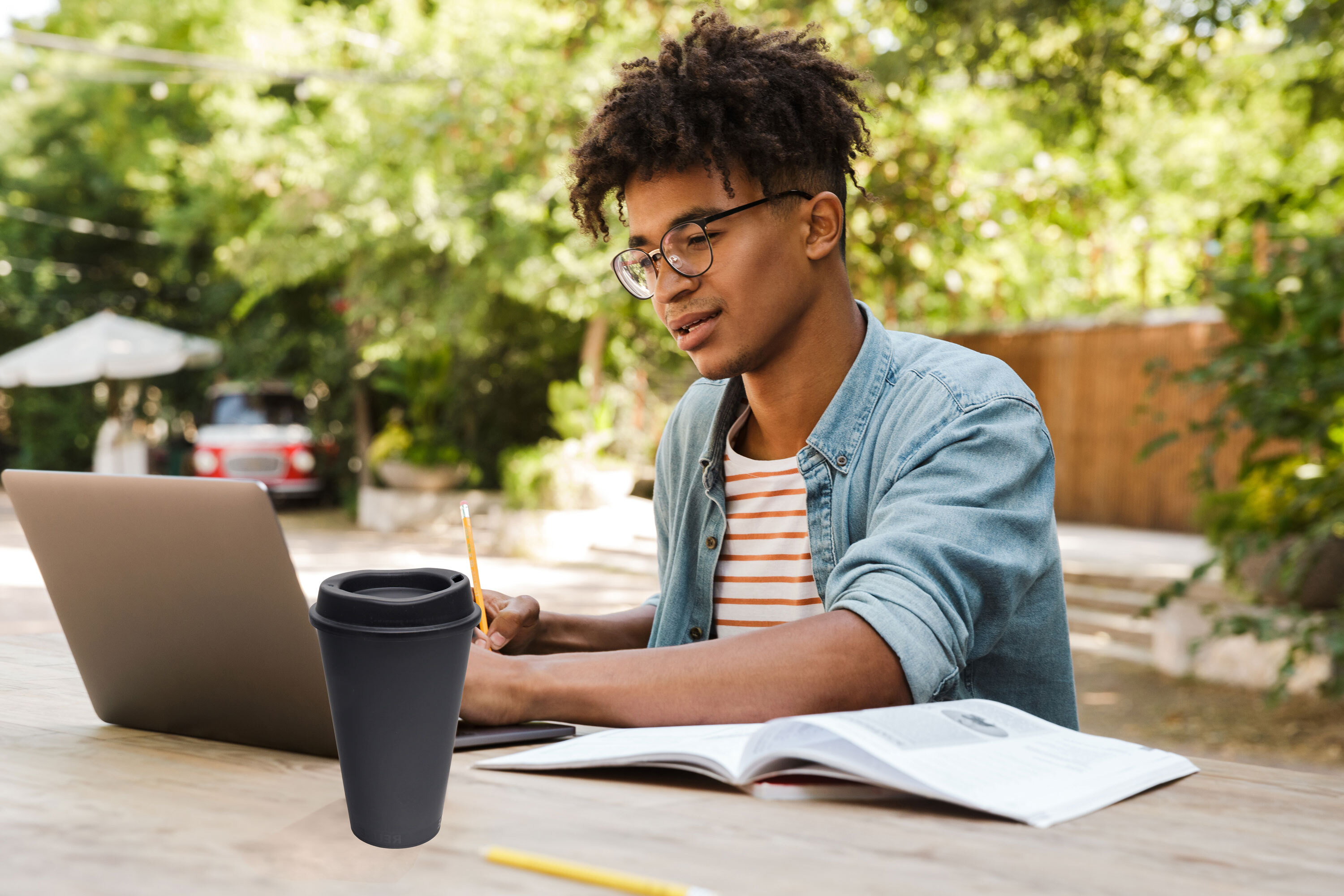 Young man studying outside with a cup of coffee.