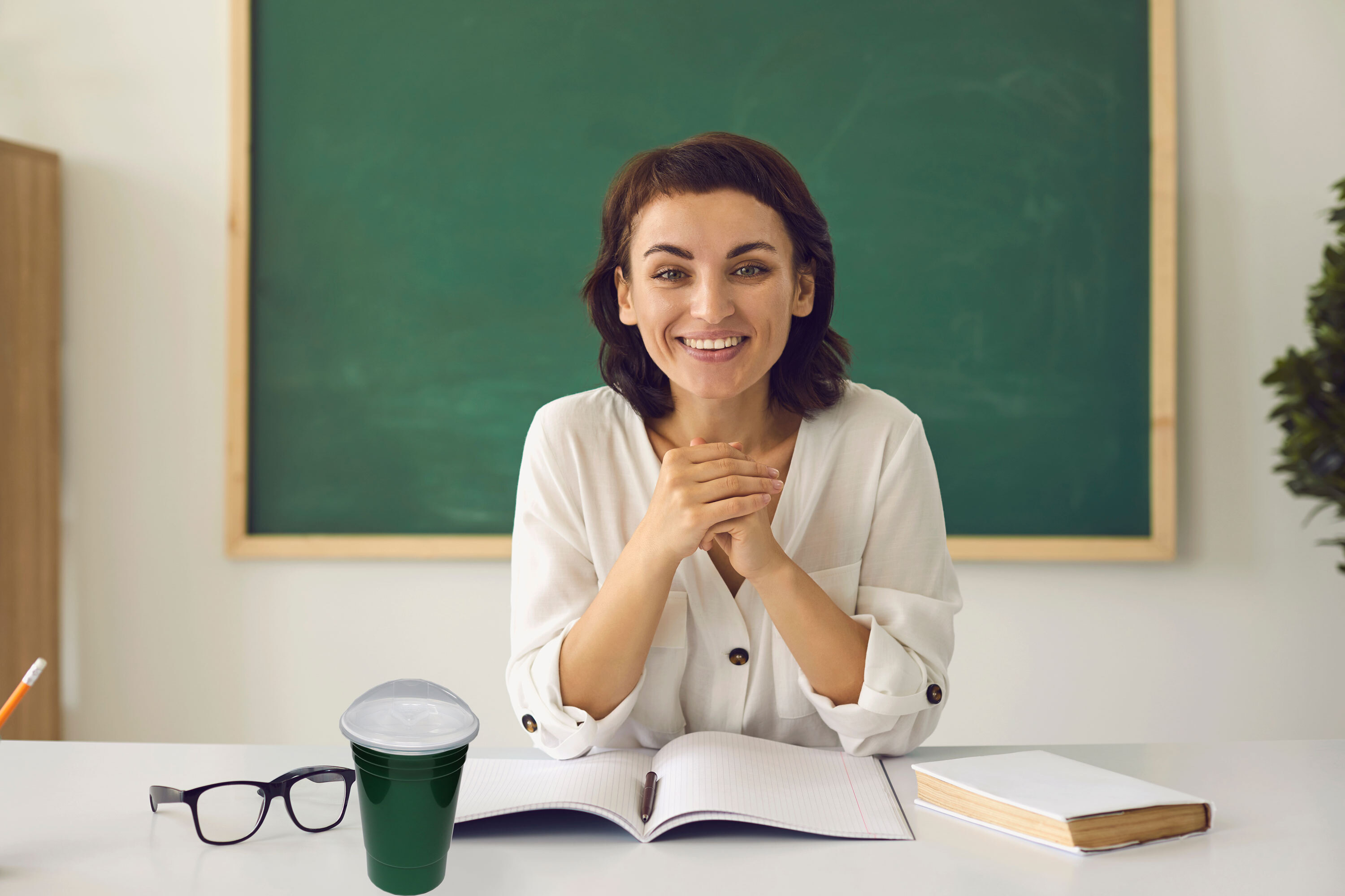 Teacher in front of chalkboard with a cup with lid.